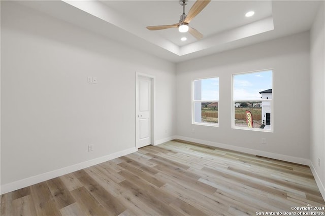 empty room featuring a raised ceiling, ceiling fan, and light hardwood / wood-style flooring