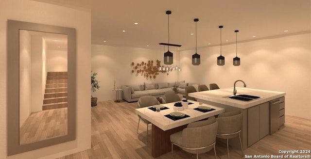 kitchen featuring a large island with sink, hanging light fixtures, sink, light wood-type flooring, and a kitchen bar