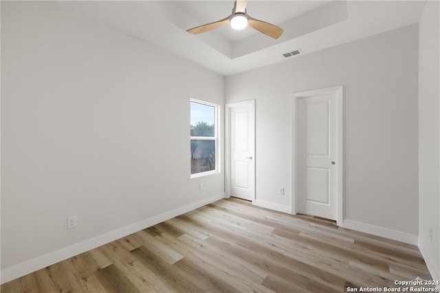 unfurnished bedroom with light wood-type flooring, a raised ceiling, and ceiling fan
