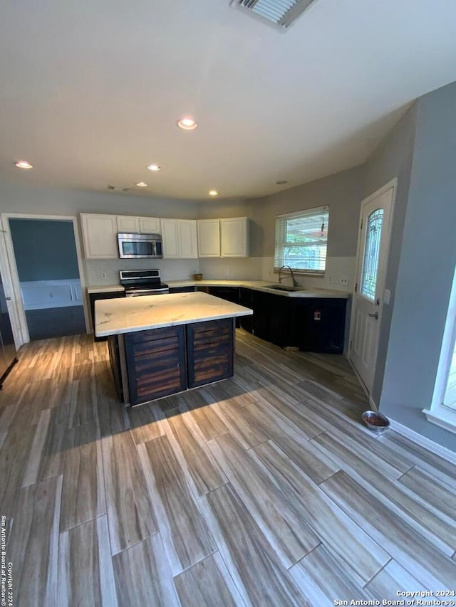 kitchen featuring white cabinetry, hardwood / wood-style flooring, sink, a kitchen island, and appliances with stainless steel finishes