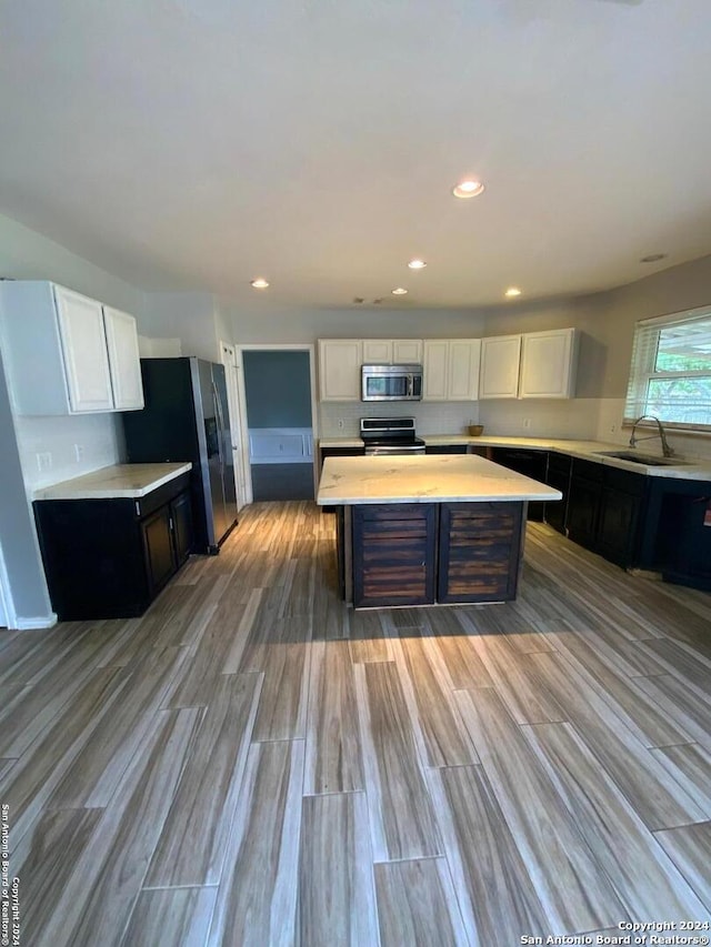 kitchen with white cabinets, a center island, appliances with stainless steel finishes, hardwood / wood-style flooring, and sink