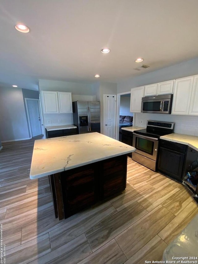 kitchen with white cabinetry, stainless steel appliances, light stone counters, and light wood-type flooring