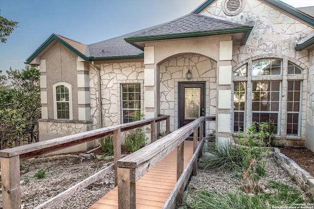 entrance to property with stone siding, a shingled roof, and stucco siding