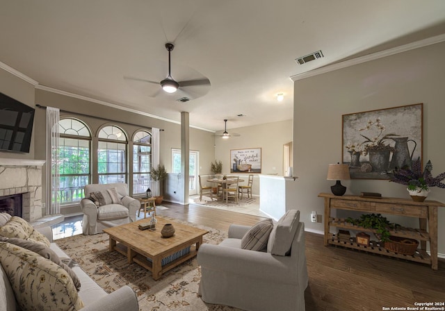 living room featuring ceiling fan, a stone fireplace, ornamental molding, and hardwood / wood-style floors