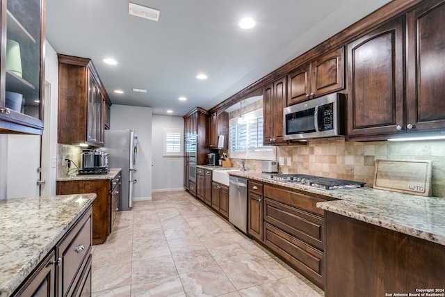 kitchen featuring appliances with stainless steel finishes, light stone counters, dark brown cabinetry, and sink