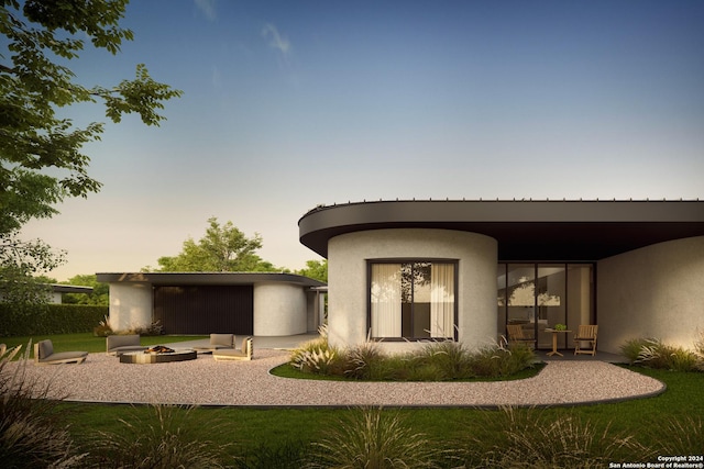 back of property at dusk featuring an outbuilding, a patio, an outdoor fire pit, and stucco siding