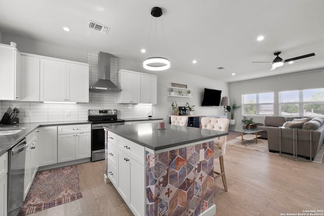 kitchen featuring stainless steel appliances, white cabinetry, wall chimney range hood, and decorative light fixtures