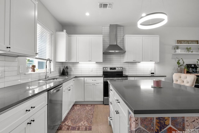 kitchen with appliances with stainless steel finishes, pendant lighting, sink, white cabinetry, and wall chimney range hood