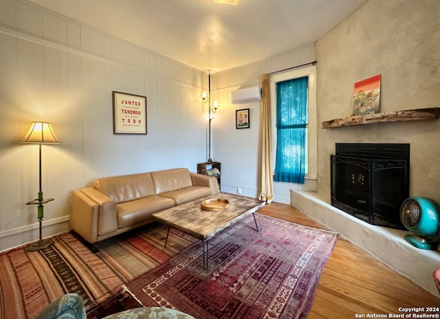 living room with a wall mounted air conditioner, a premium fireplace, and wood-type flooring