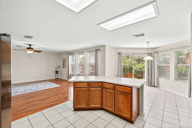 kitchen with brown cabinetry, light countertops, a kitchen island, and visible vents