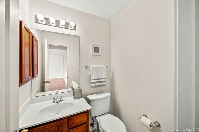 bathroom with a textured wall, vanity, and toilet