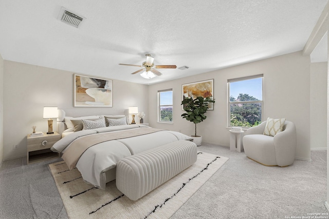 bedroom featuring a ceiling fan, visible vents, a textured ceiling, and light colored carpet