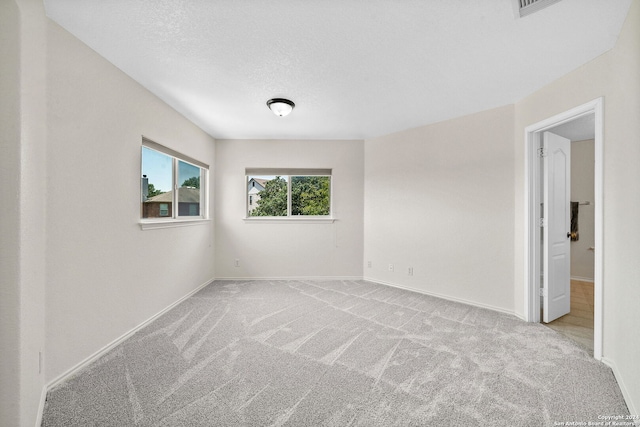 unfurnished room featuring light colored carpet, a textured ceiling, and baseboards