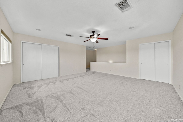 unfurnished bedroom with light carpet, two closets, visible vents, and a ceiling fan