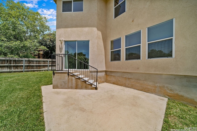 view of exterior entry with stucco siding, fence, a lawn, and a patio