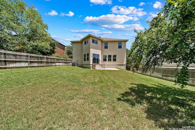 rear view of property with a fenced backyard, a lawn, central AC unit, and stucco siding