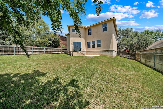 rear view of property featuring a lawn, a fenced backyard, and stucco siding