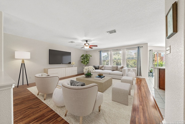 living area featuring a ceiling fan, a textured ceiling, visible vents, and wood finished floors