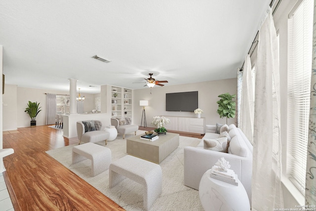 living room featuring light wood-style floors, built in shelves, visible vents, and ceiling fan with notable chandelier