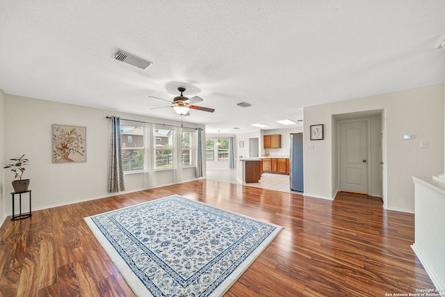 living area with ceiling fan, a textured ceiling, wood finished floors, visible vents, and baseboards