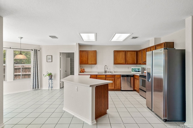 kitchen featuring brown cabinets, decorative light fixtures, stainless steel appliances, light countertops, and a sink