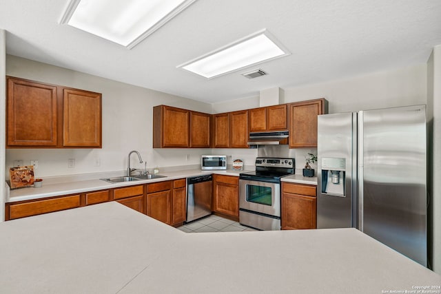 kitchen with appliances with stainless steel finishes, brown cabinets, light countertops, under cabinet range hood, and a sink