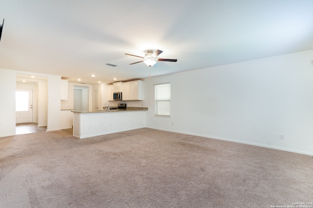 unfurnished living room with sink, ceiling fan, and light colored carpet