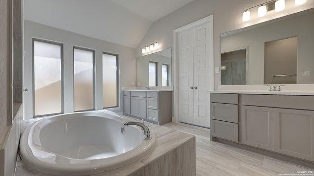 bathroom featuring tiled tub, vaulted ceiling, and vanity