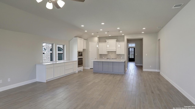 kitchen featuring oven, white cabinetry, decorative backsplash, a kitchen island with sink, and built in microwave