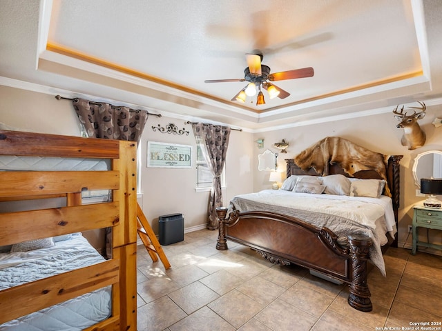 tiled bedroom featuring ornamental molding, ceiling fan, and a tray ceiling