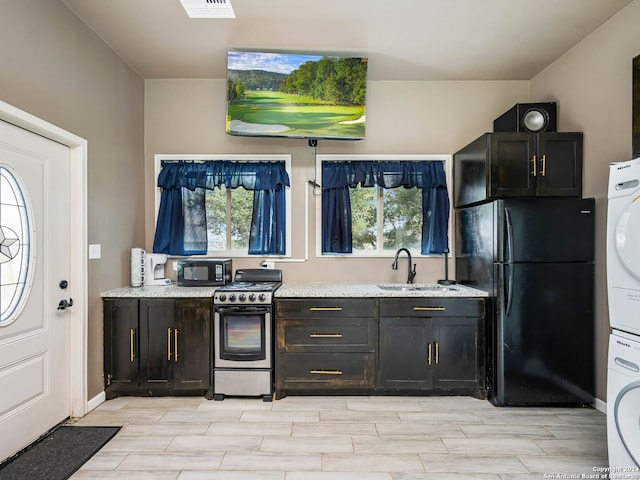 kitchen featuring sink, light stone countertops, black appliances, and stacked washer / drying machine