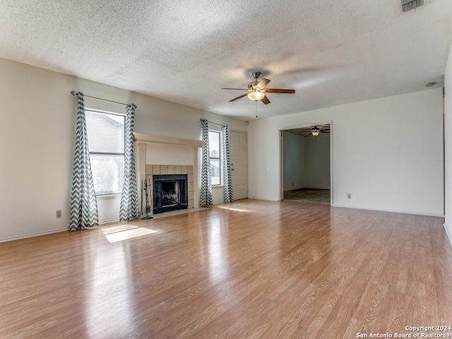 unfurnished living room with light hardwood / wood-style floors, a tile fireplace, ceiling fan, and a textured ceiling