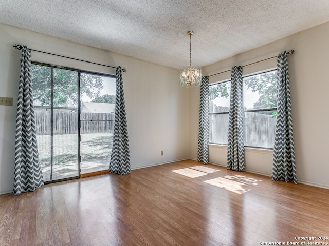 empty room with a textured ceiling, a notable chandelier, wood-type flooring, and a healthy amount of sunlight