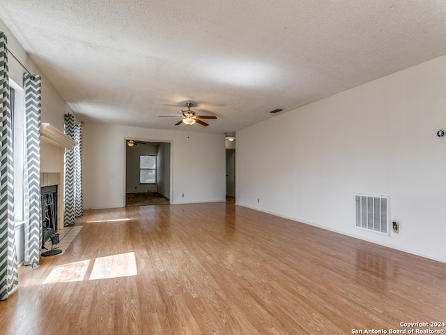 unfurnished living room with a fireplace, light wood-type flooring, ceiling fan, and a textured ceiling