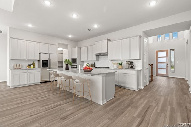 kitchen featuring stainless steel refrigerator with ice dispenser, a kitchen bar, white cabinetry, and an island with sink