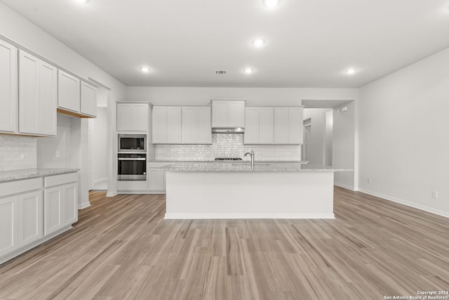 kitchen with a center island with sink, stainless steel appliances, light stone countertops, white cabinets, and light hardwood / wood-style flooring