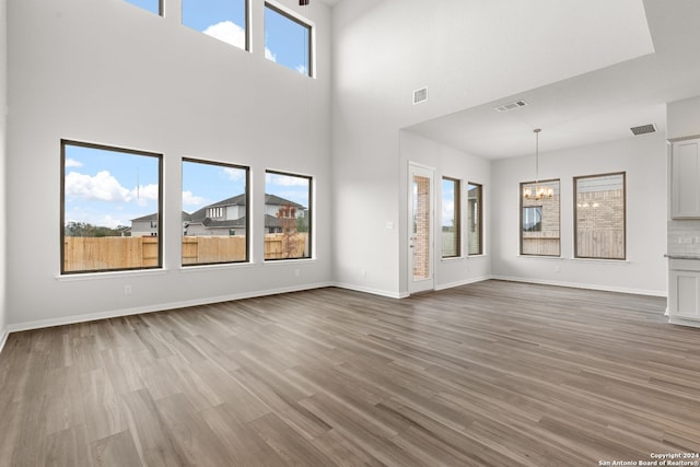 unfurnished living room featuring a towering ceiling, hardwood / wood-style flooring, an inviting chandelier, and plenty of natural light