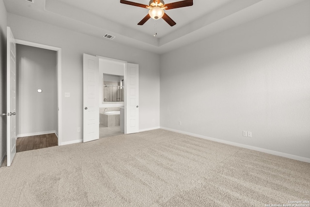 unfurnished bedroom with a raised ceiling, ceiling fan, carpet, and connected bathroom