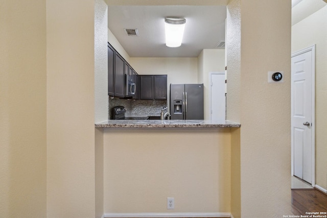 kitchen with dark brown cabinetry, appliances with stainless steel finishes, kitchen peninsula, light stone countertops, and decorative backsplash