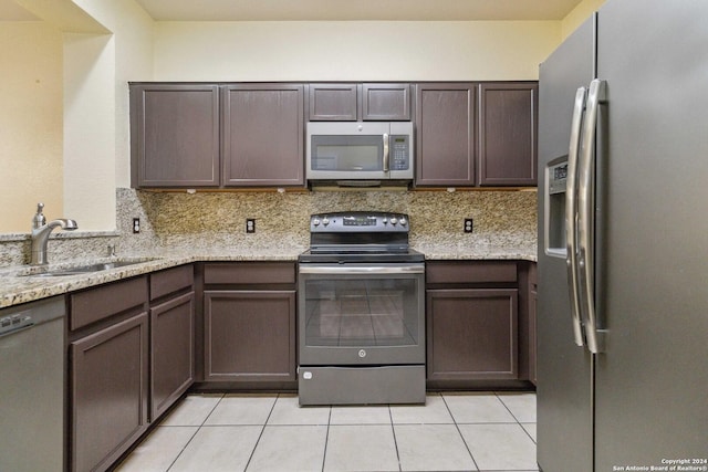 kitchen with light tile patterned flooring, appliances with stainless steel finishes, tasteful backsplash, sink, and light stone countertops