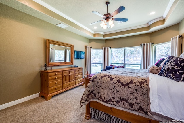 bedroom featuring a tray ceiling, crown molding, a ceiling fan, light carpet, and baseboards