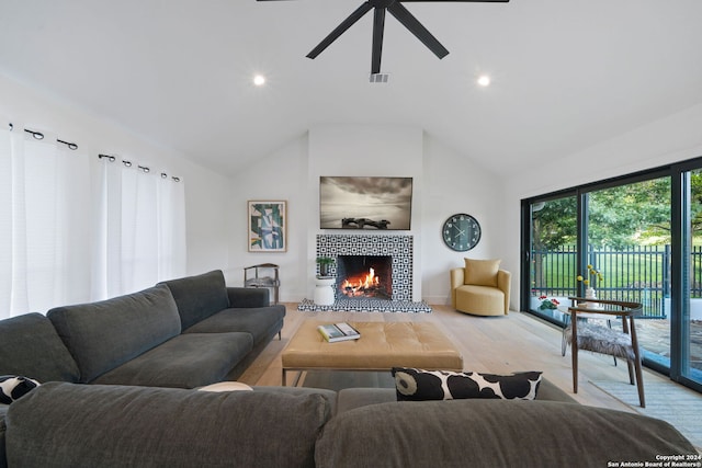 living room featuring vaulted ceiling, ceiling fan, light hardwood / wood-style floors, and a tiled fireplace