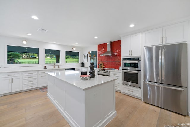 kitchen with wall chimney range hood, light hardwood / wood-style floors, white cabinets, and appliances with stainless steel finishes