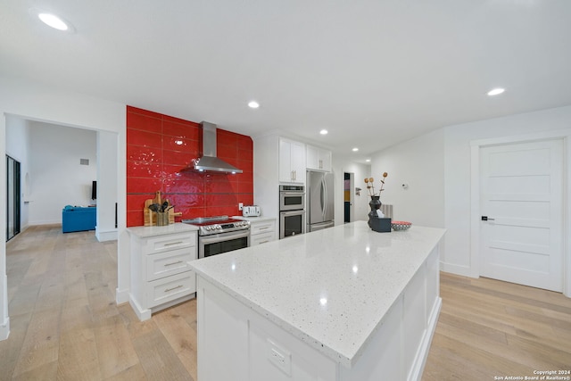 kitchen with appliances with stainless steel finishes, a center island, white cabinetry, wall chimney range hood, and tasteful backsplash