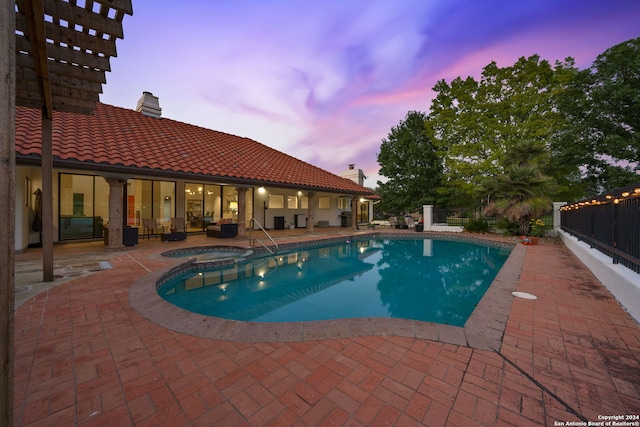 pool at dusk featuring an in ground hot tub and a patio