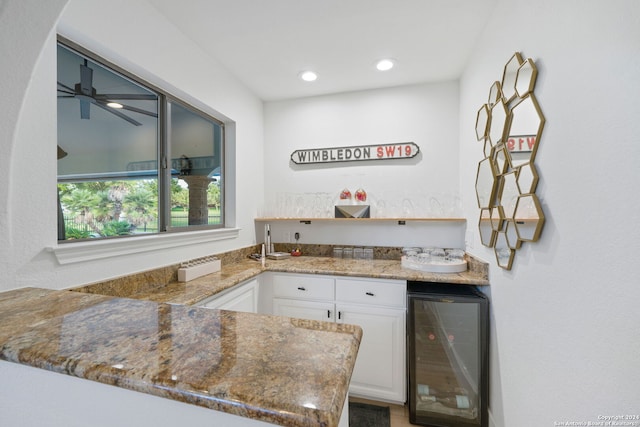 bar with dark stone counters, white cabinetry, ceiling fan, and beverage cooler