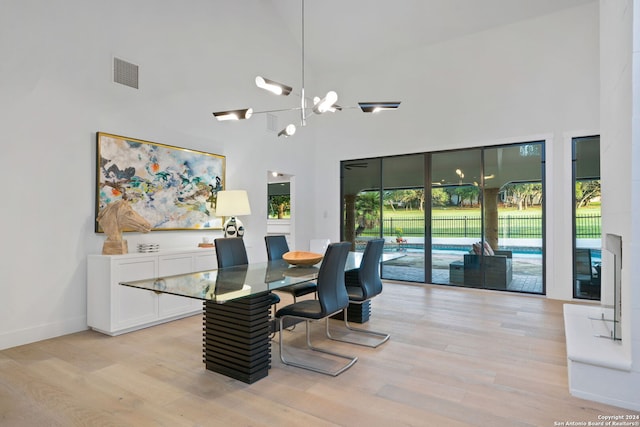 dining area featuring light wood-type flooring, a towering ceiling, and a chandelier