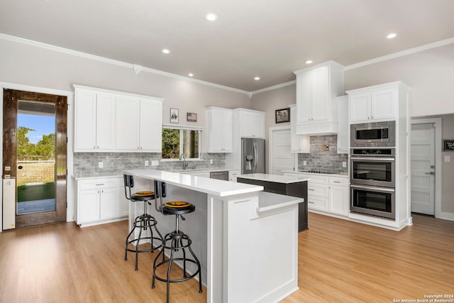 kitchen featuring white cabinets, appliances with stainless steel finishes, a kitchen breakfast bar, a center island, and light countertops