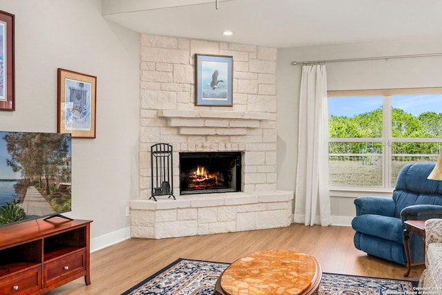 living room with light wood-type flooring, a stone fireplace, and baseboards