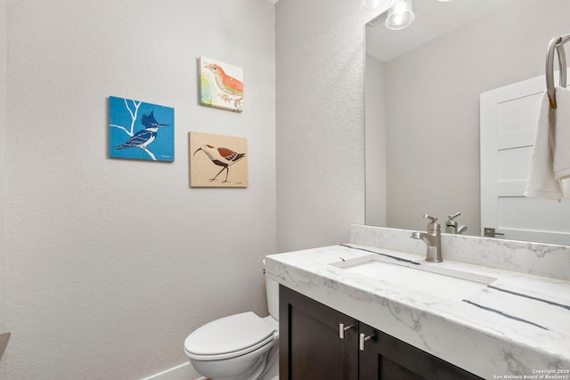 half bath with toilet, a textured wall, and vanity